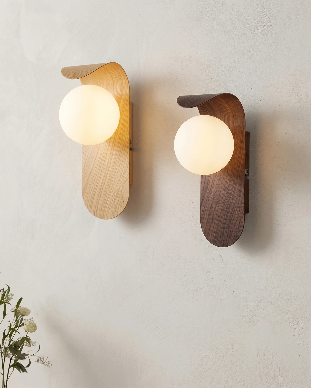 Two wood wall sconces RIMINI No.01 lit side by side on a plaster wall, one in natural wood and one in walnut