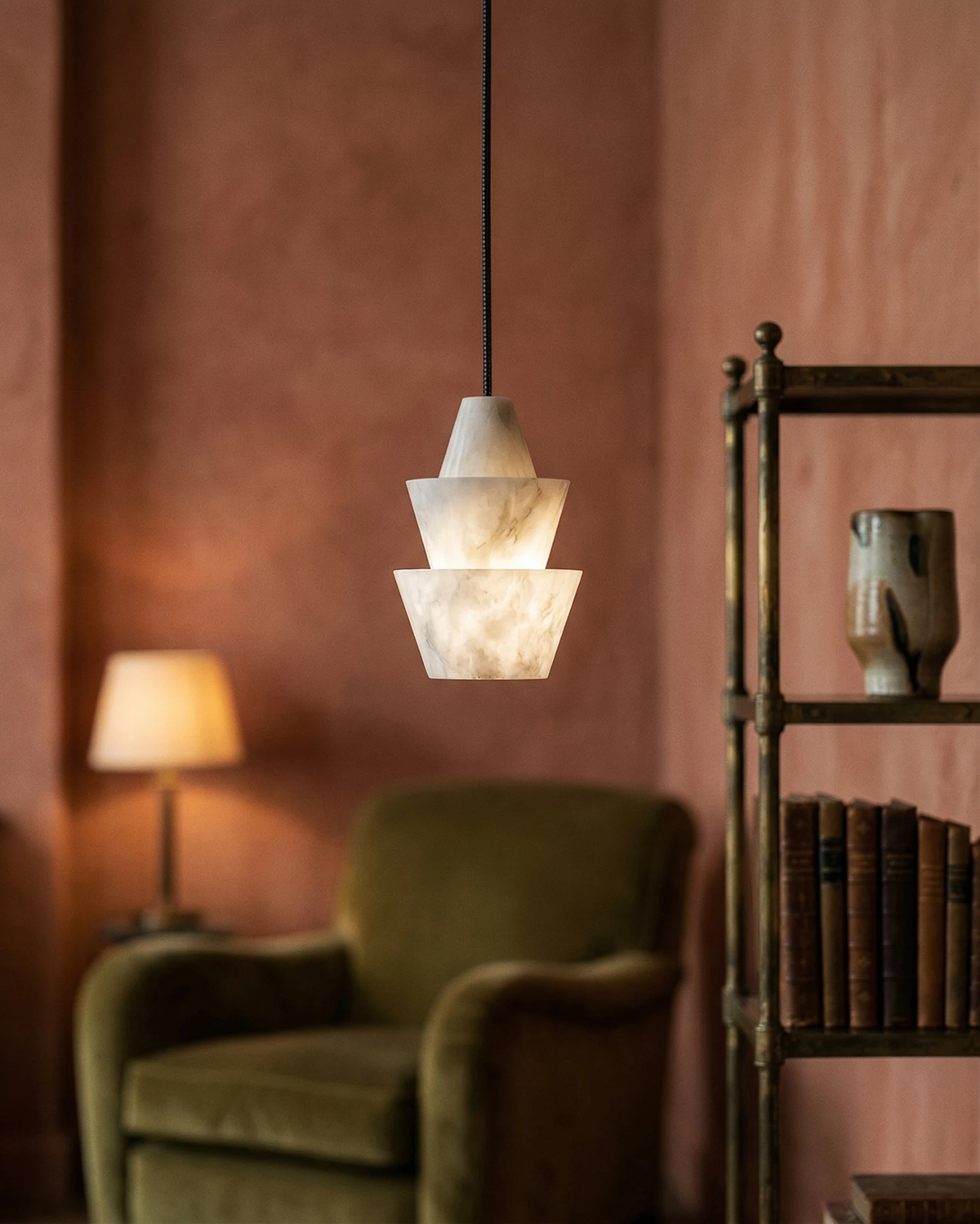 Alabaster pendant light ALABA No.06 lit above an olive velvet armchair beside a bookshelf and a table lamp