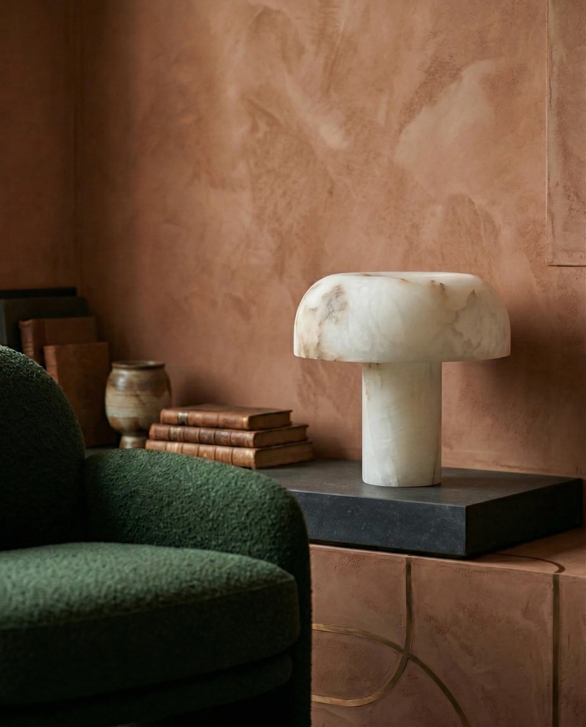 Alabaster table lamp OBSI No.01 on a black side table beside a green armchair against terracotta walls