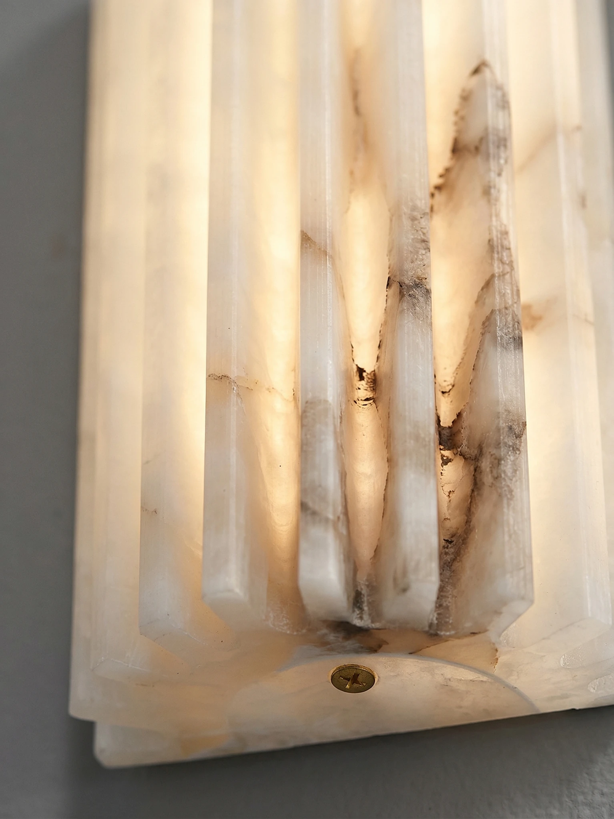 Close-up of the lit fluted alabaster of the ALABA No.02 wall sconce showing the gray veining and a brass screw