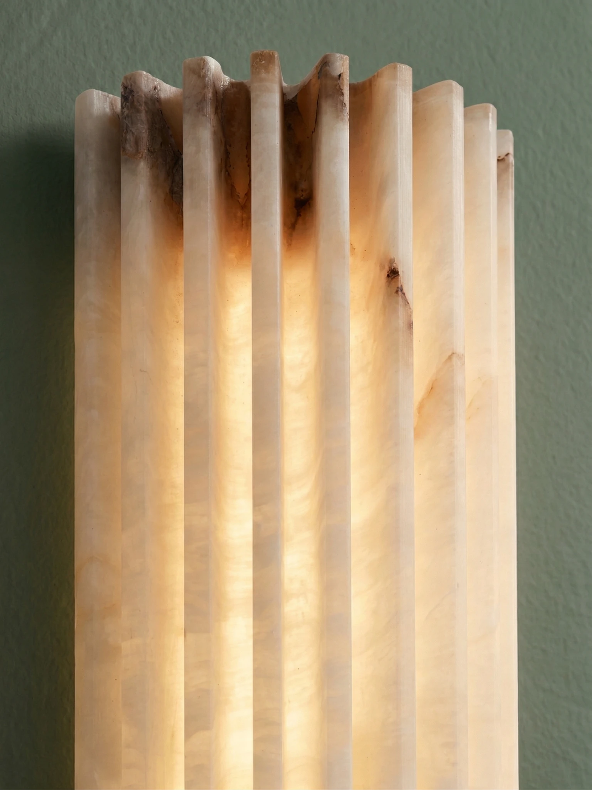 Close-up of the ALABA No.02 alabaster wall sconce ribs glowing against a dark green wall