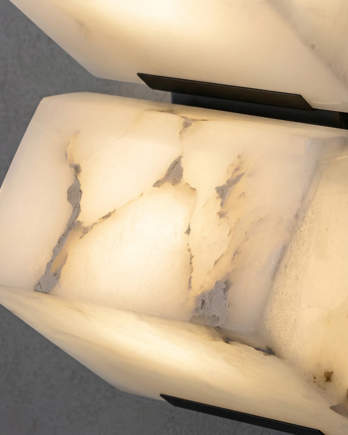 Close-up of the faceted alabaster of the ALABA No.05 wall sconce, veined stone glowing when switched on