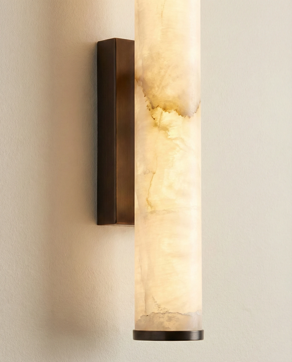 Close-up of the NEBBIA No.01 alabaster wall sconce, glowing translucent tube on a Dark Bronze bracket