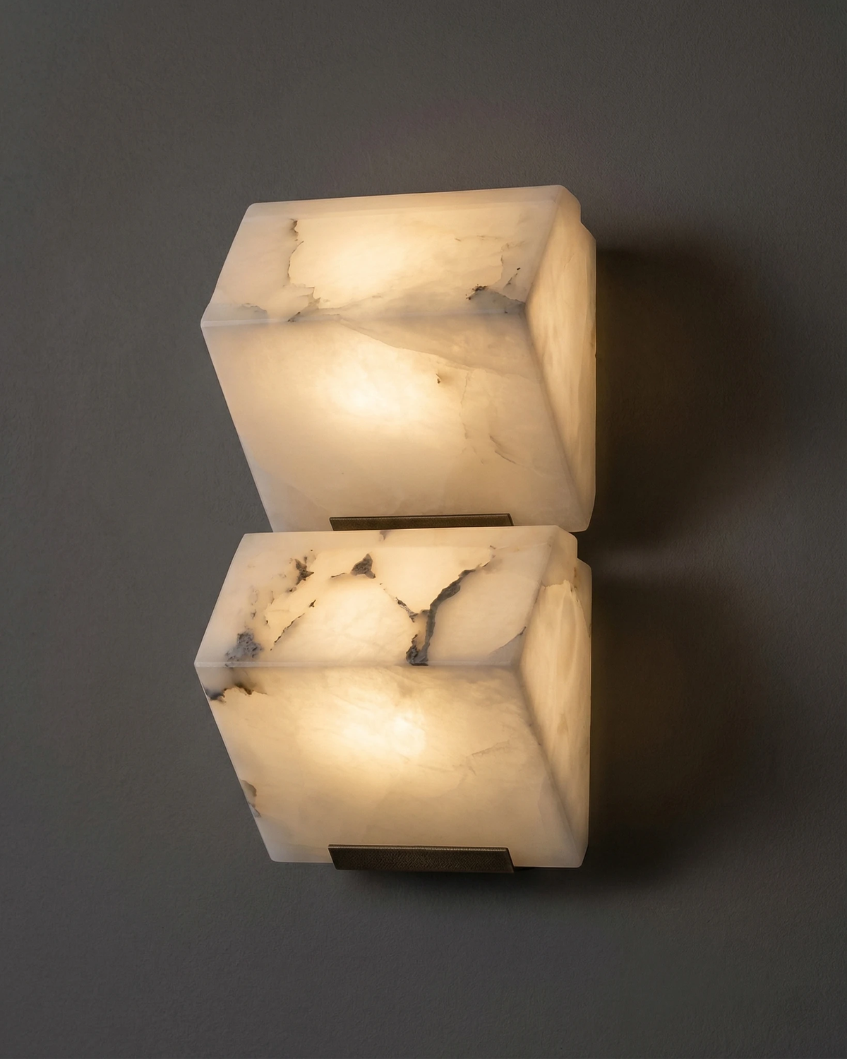Close-up of the ALABA No.05 alabaster wall sconce duo, two faceted blocks glowing with visible grey veining