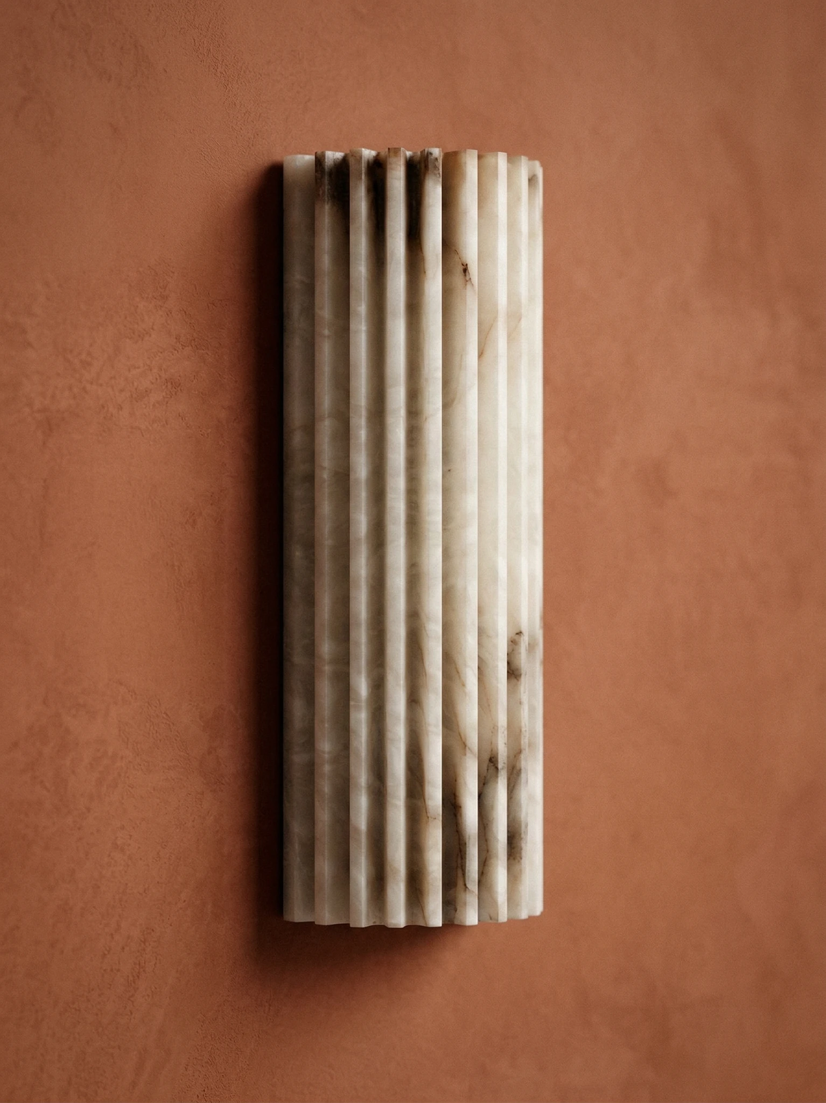 Alabaster wall sconce ALABA No.02 mounted on a terracotta plaster wall, fluted stone column lit from within