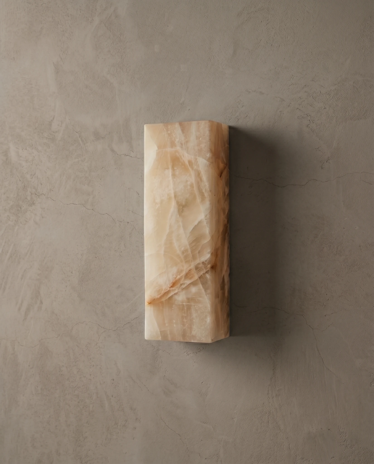 Alabaster wall sconce ALABA No.03 switched on against a textured plaster wall, veined alabaster block