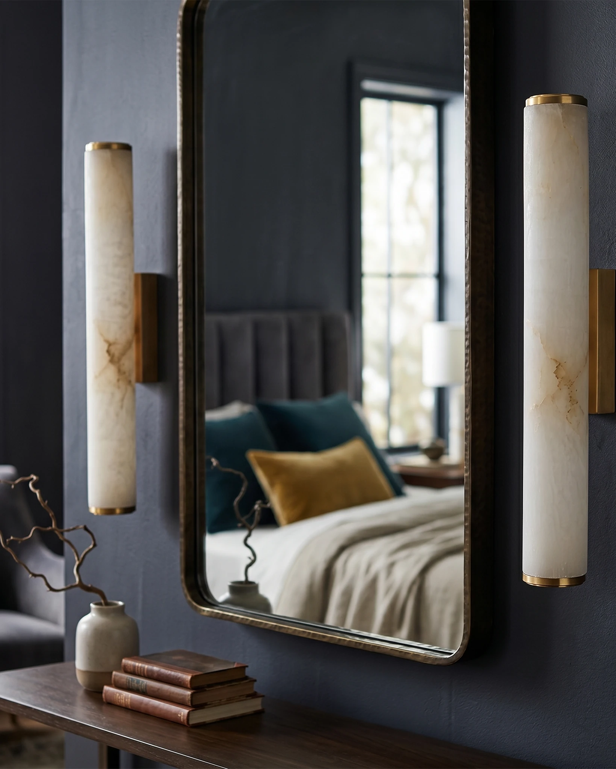 Two alabaster wall sconces NEBBIA No.01 on Warm Gold brackets flanking a mirror on a navy wall, bed reflected