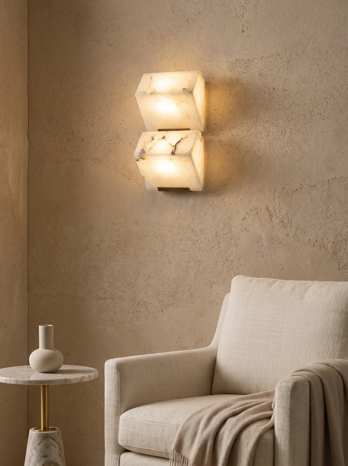 Alabaster wall sconce ALABA No.05 duo switched on above a cream armchair with a throw on a plaster wall