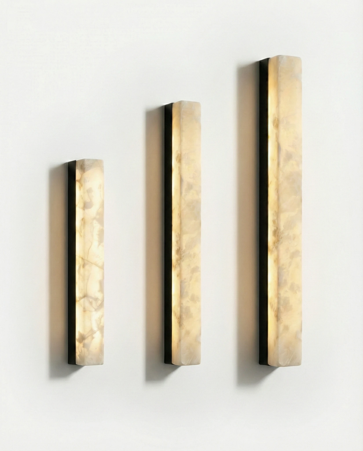 Three alabaster wall sconces NEBBIA No.02 in three sizes side by side on Volcano Black bars, all switched on