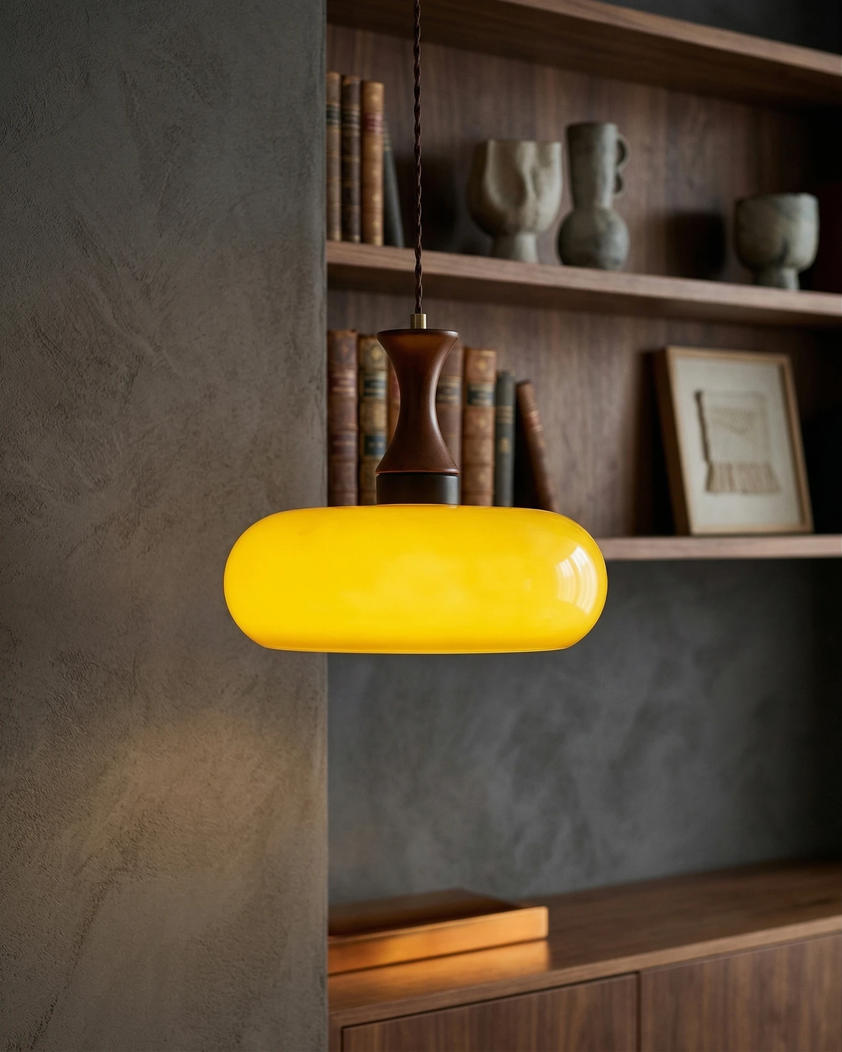 Amber glass pendant light OVIA No.04, disc shade glowing bright yellow in front of walnut bookshelves