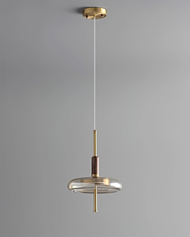 Amber glass pendant light NOCE No.01 hanging on a long cable from a brass canopy against a gray wall, lit