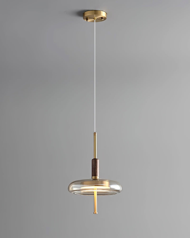 Amber glass pendant light NOCE No.01 on a shorter drop from a brass ceiling canopy, glass disc lit, gray wall