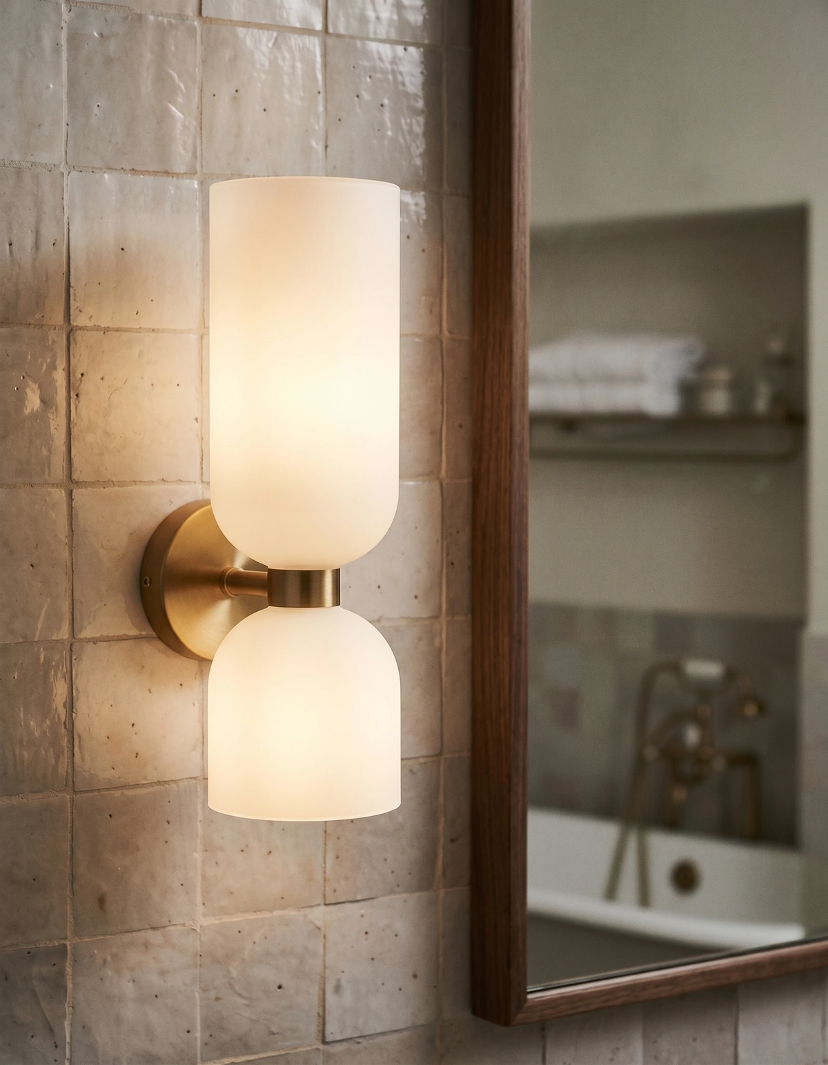 Brass wall sconce DALIA No.01, twin opal shades glowing on beige zellige tile next to a walnut-framed mirror