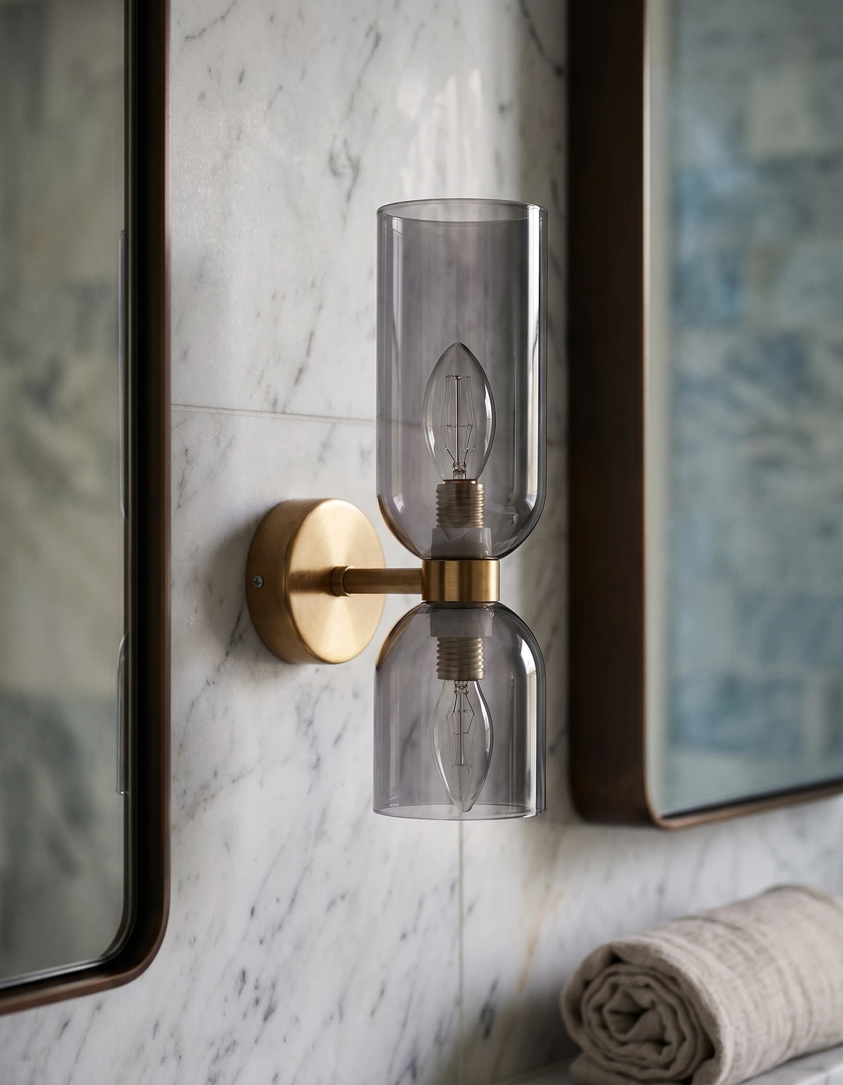 Brass wall sconce DALIA No.01 with smoked glass mounted between two mirrors on a white marble bathroom wall