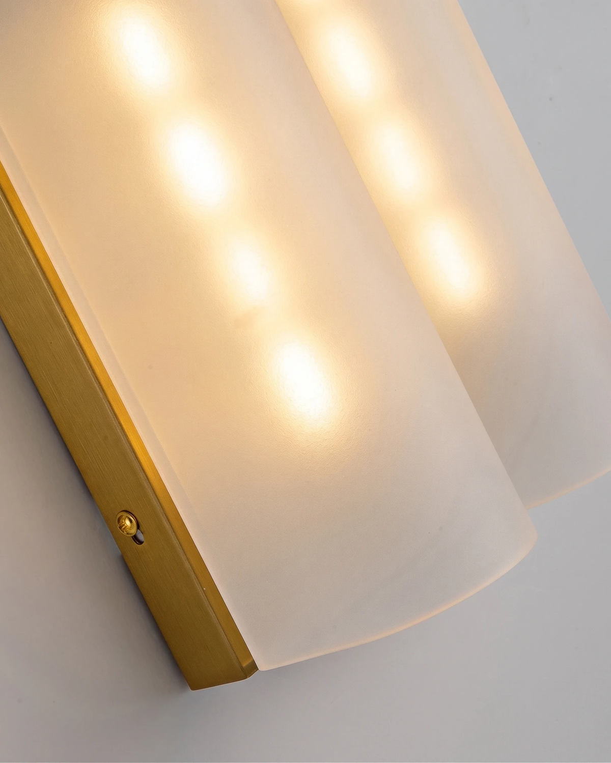Close-up of the lit frosted glass shield with brass edge of the PILA No.01 brass wall sconce showing LED points