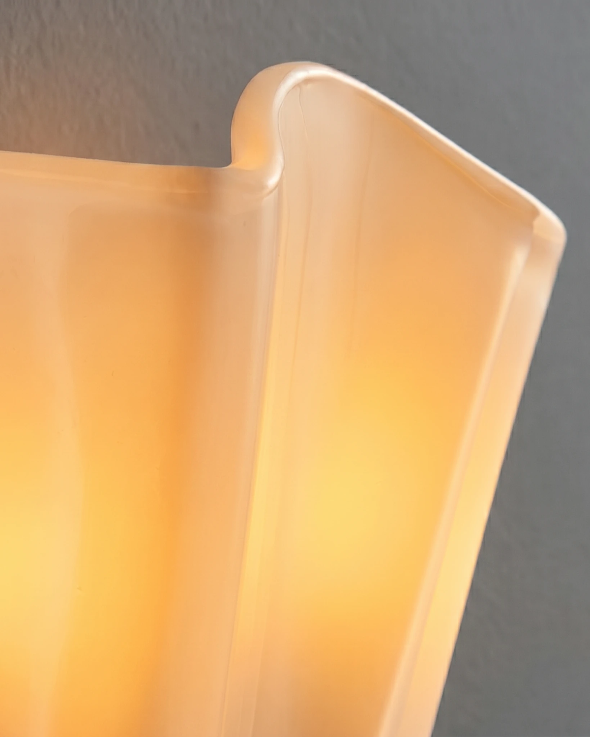 Close-up of the lit ivory blown-glass corolla of the brass wall sconce DALIA No.03 showing its wavy edge