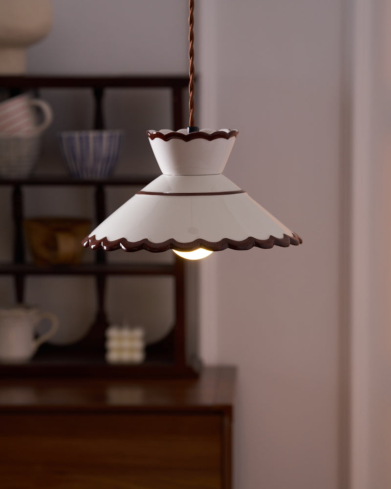Ceramic pendant light MELI No.04 switched on over a wooden sideboard with a bowl and shelved dishes