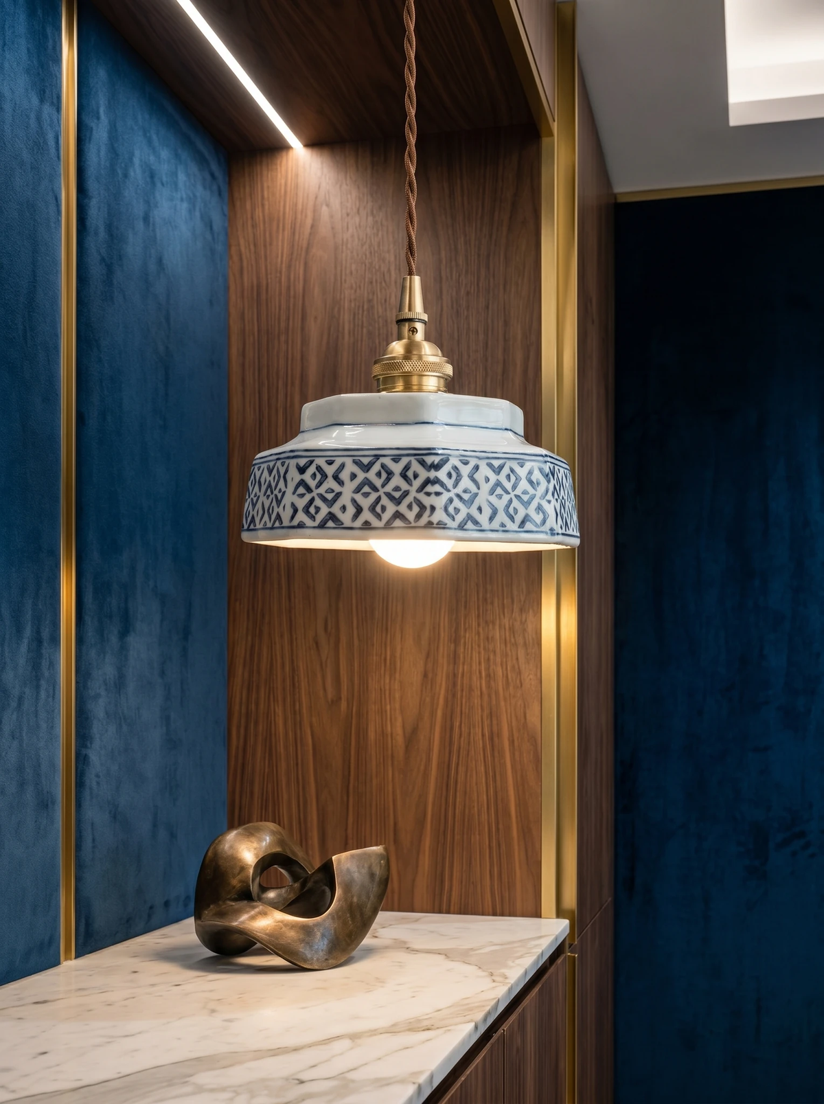 Ceramic pendant light RAGUSA No.02 lit above a marble console in a walnut and blue velvet niche with a bronze sculpture