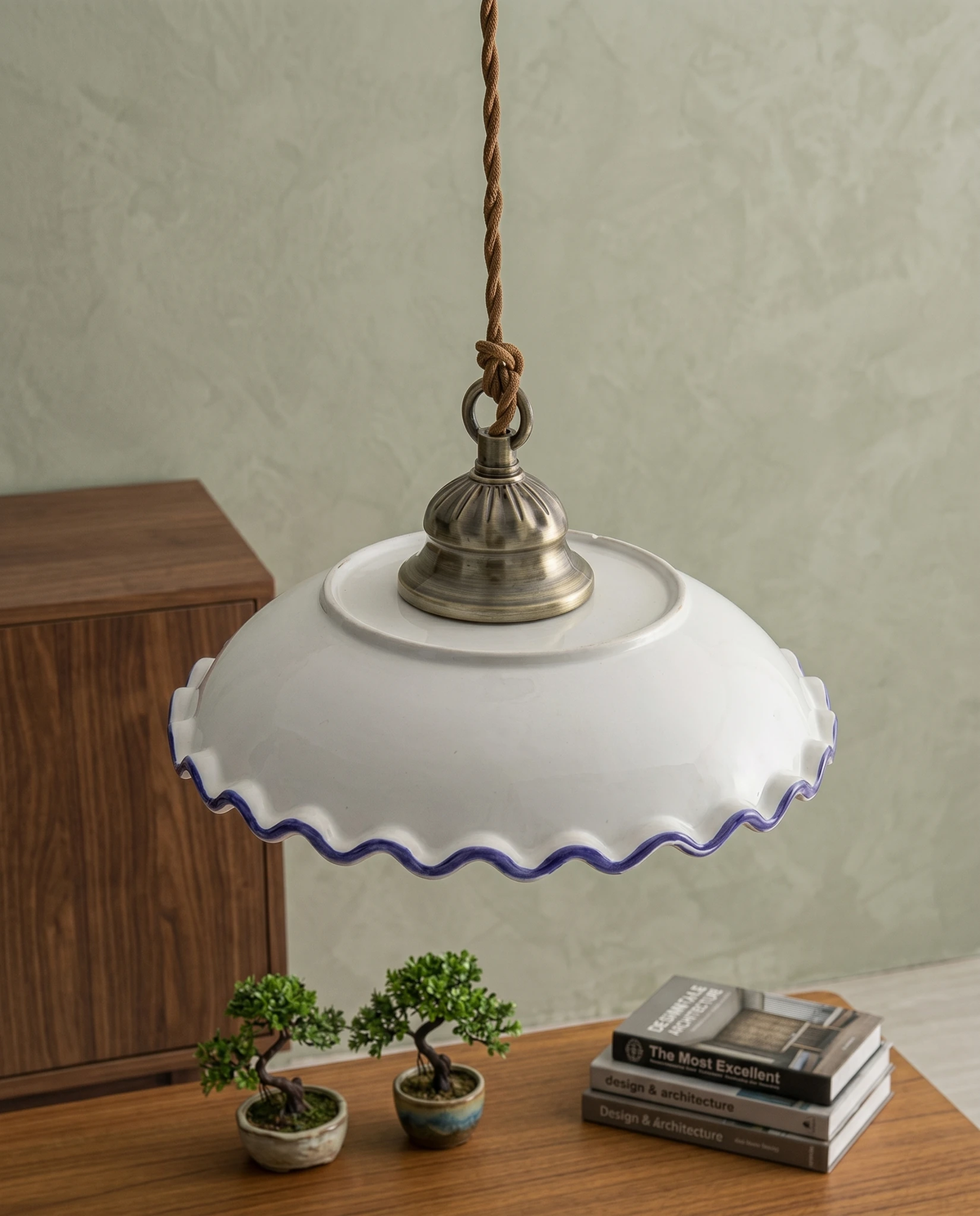 Ceramic pendant light MELI No.01 with a scalloped blue rim hung low over a walnut sideboard with bonsai and books