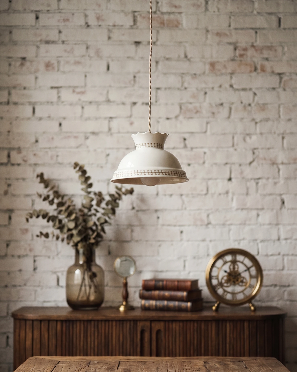 Ceramic pendant light TERRA No.01 lit above a wood console with books and a clock against a white brick wall