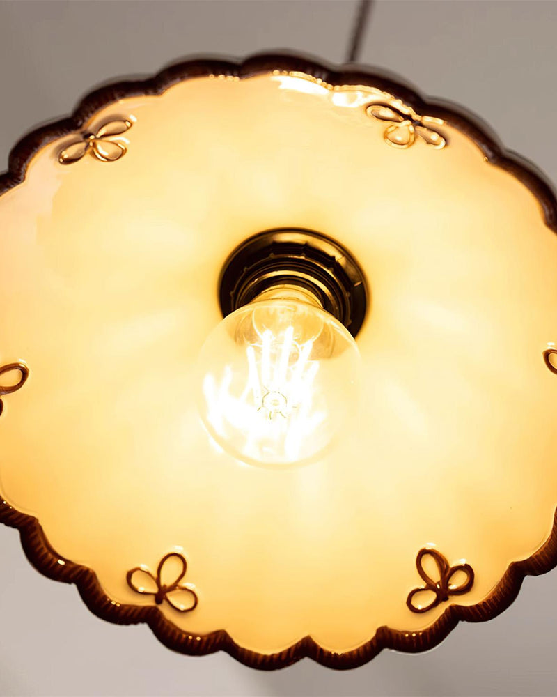 Close-up from below of the lit ceramic pendant light MELI No.04 showing the bulb and painted bow motifs