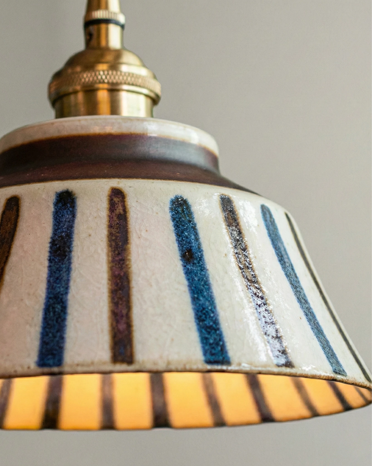 Close-up of the blue striped bell with brown rim and brass socket of the MELI No.05 ceramic pendant light, lit