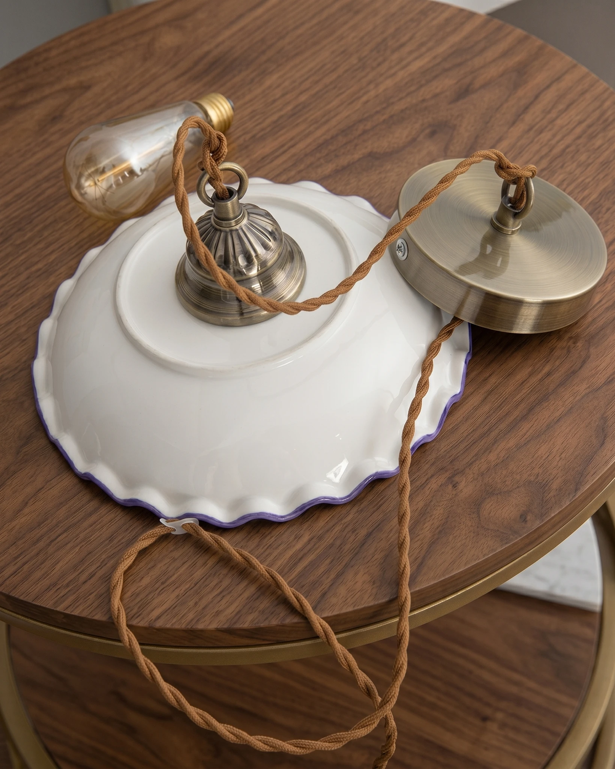 Close-up of the ceramic pendant light MELI No.01 laid on a walnut table with its brass canopy, twisted cord and bulb