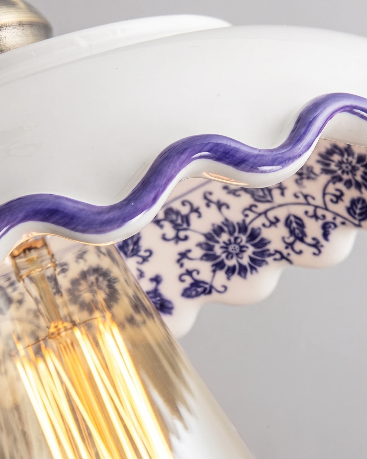 Close-up of the scalloped edge of the ceramic pendant light MELI No.01 with blue floral painting and a lit bulb
