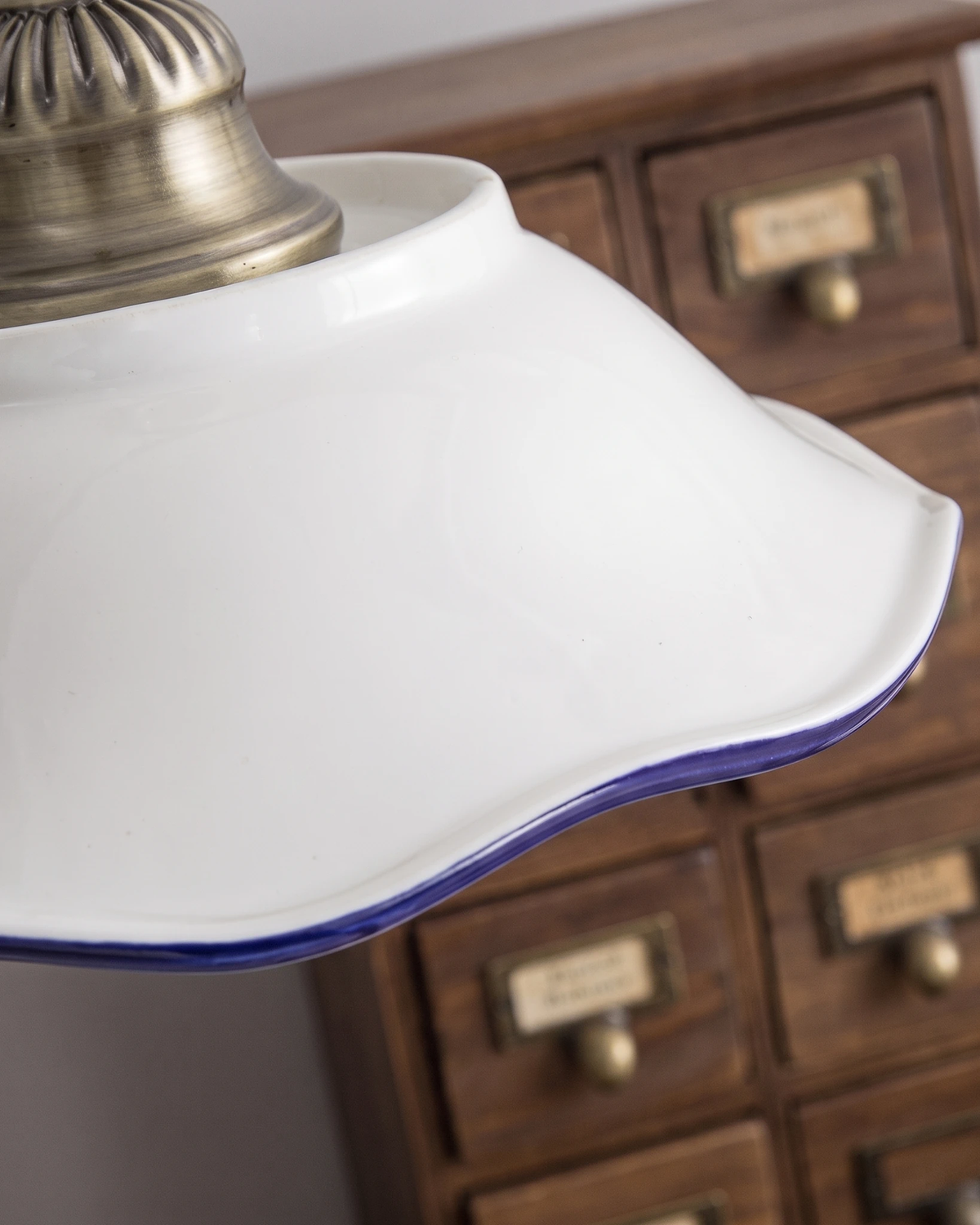 Close-up of the ceramic pendant light MELI No.01 shade with its blue painted rim above wooden apothecary drawers