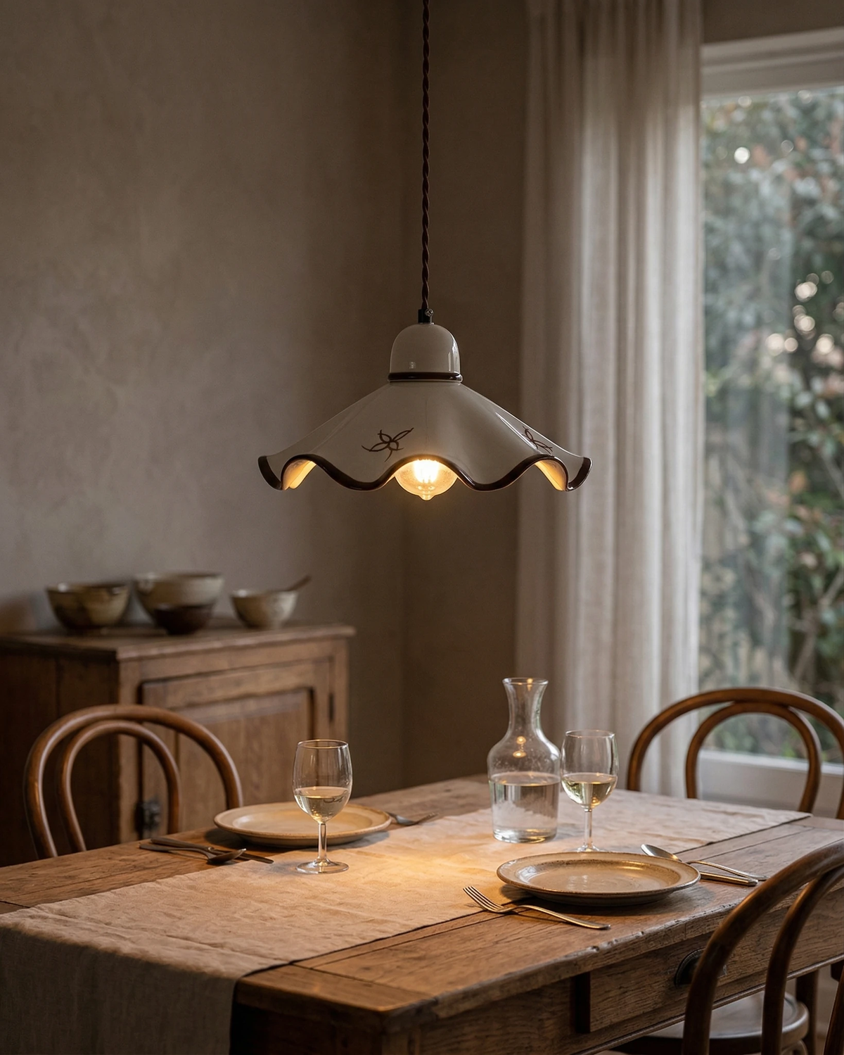 Ceramic pendant light CAPRI No.01 lit low over a rustic wood dining table set with bowls and glasses