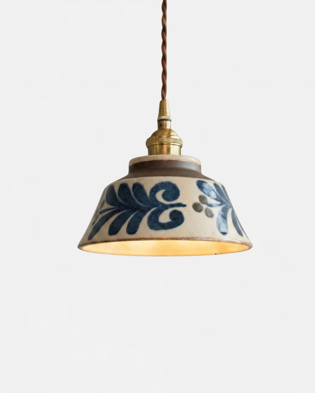 Ceramic pendant light MELI No.05 in Azure Eden, blue scrolling leaf motif on a white bell with brass cap, lit