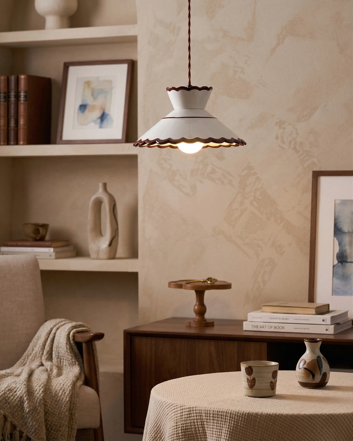Ceramic pendant light MELI No.04 in cream white lit above a round cloth-covered table with shelves behind