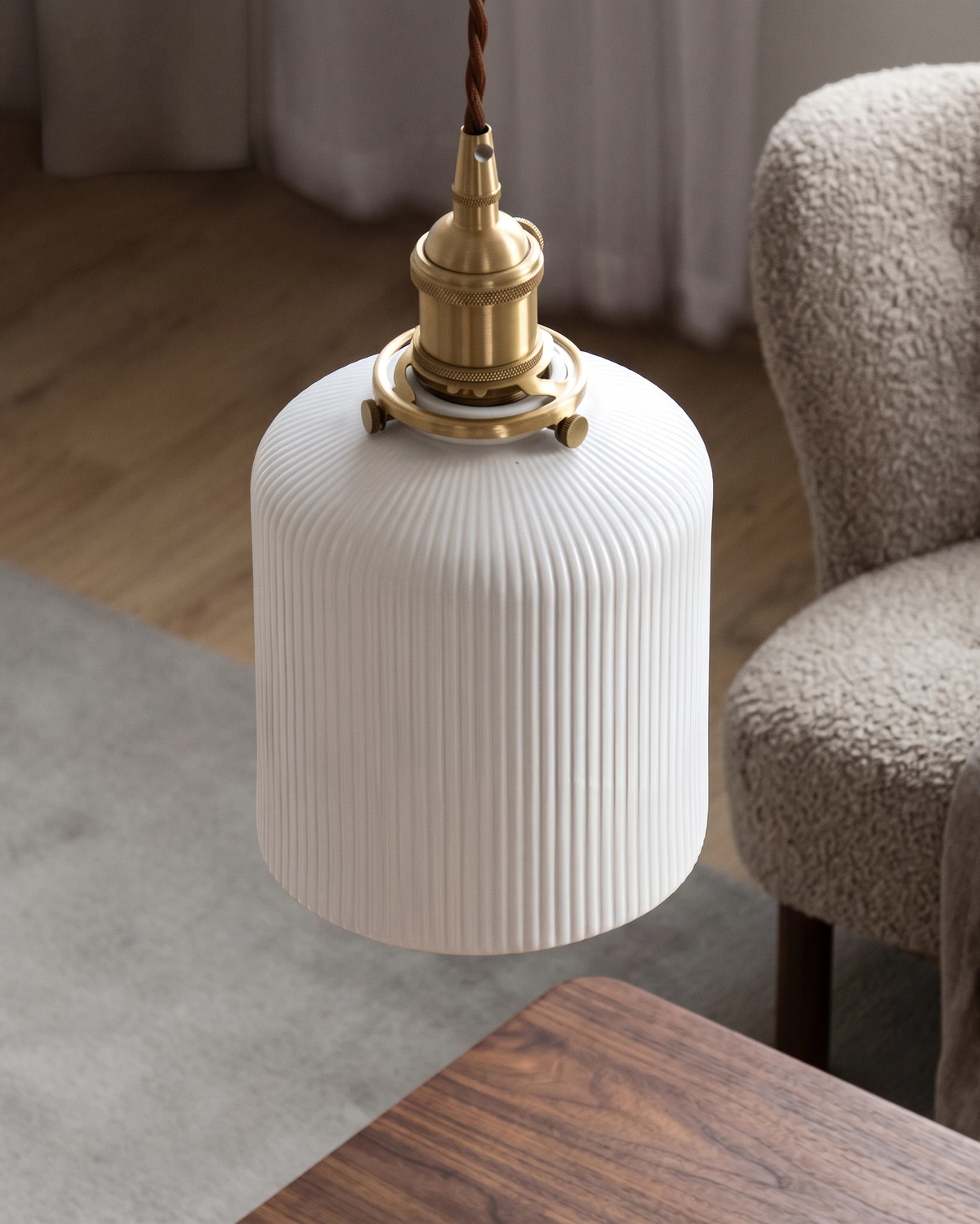 Ceramic pendant light SERA No.01 cylinder shade hung low over a walnut table next to a boucle armchair, unlit