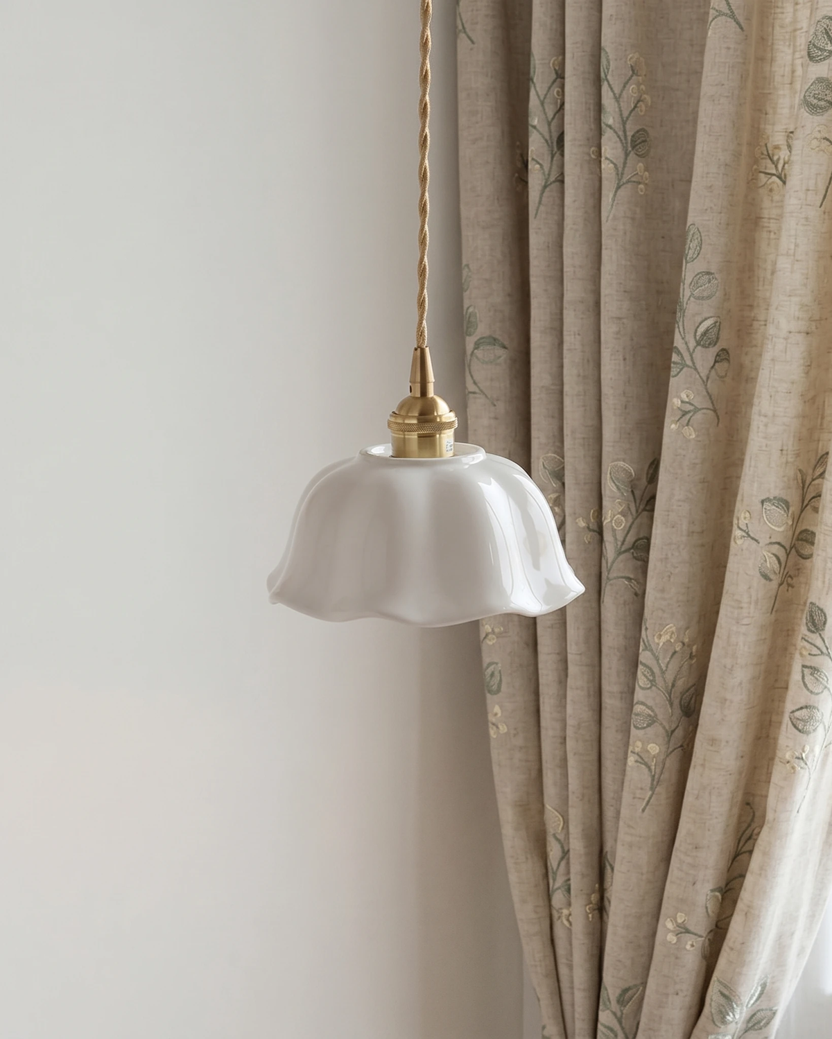 Ceramic pendant light MELI No.03 hanging unlit beside an embroidered linen curtain, brass socket on a twisted cord