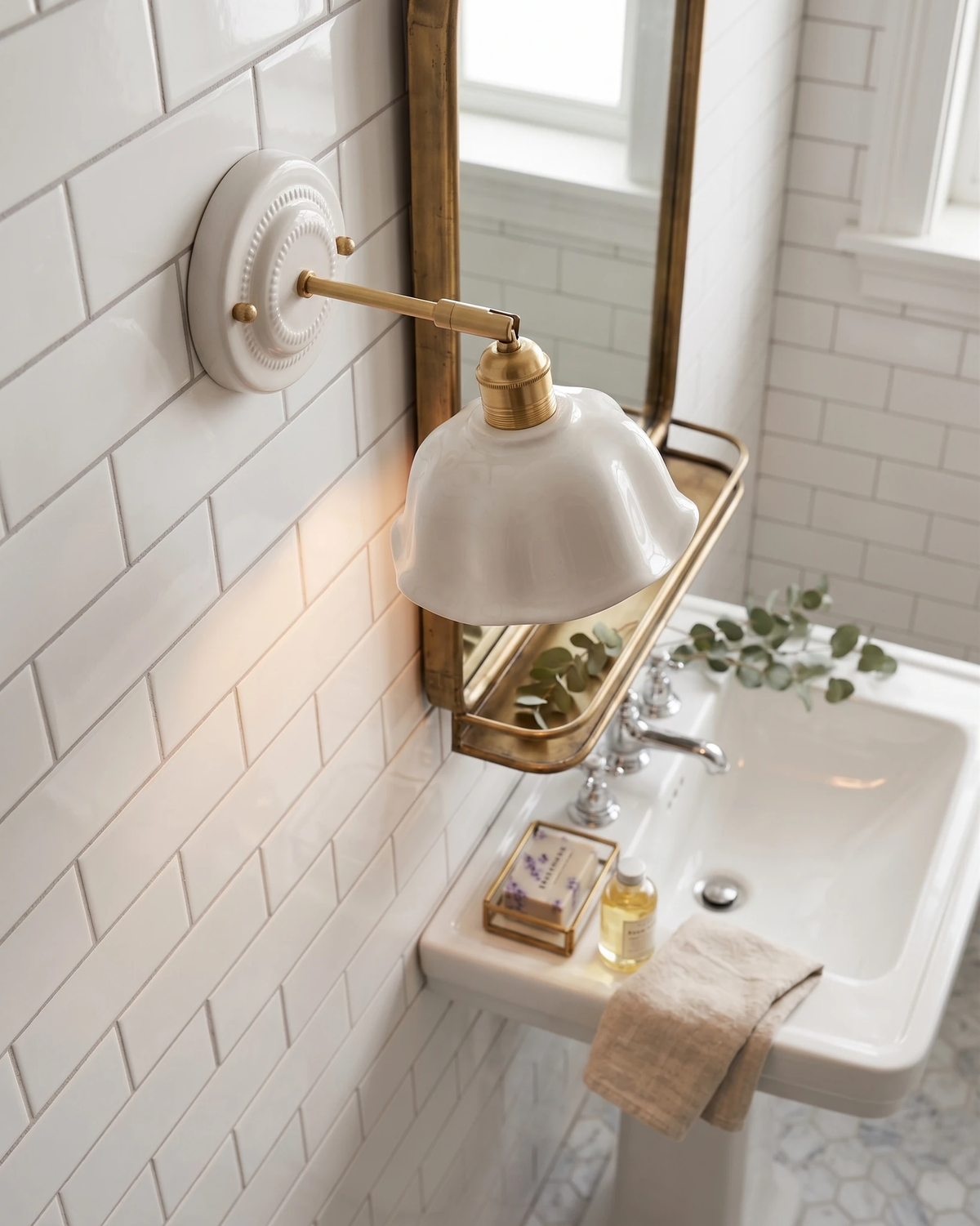 Ceramic wall sconce RIGA No.05 lit on white subway tile above a pedestal sink with a brass mirror