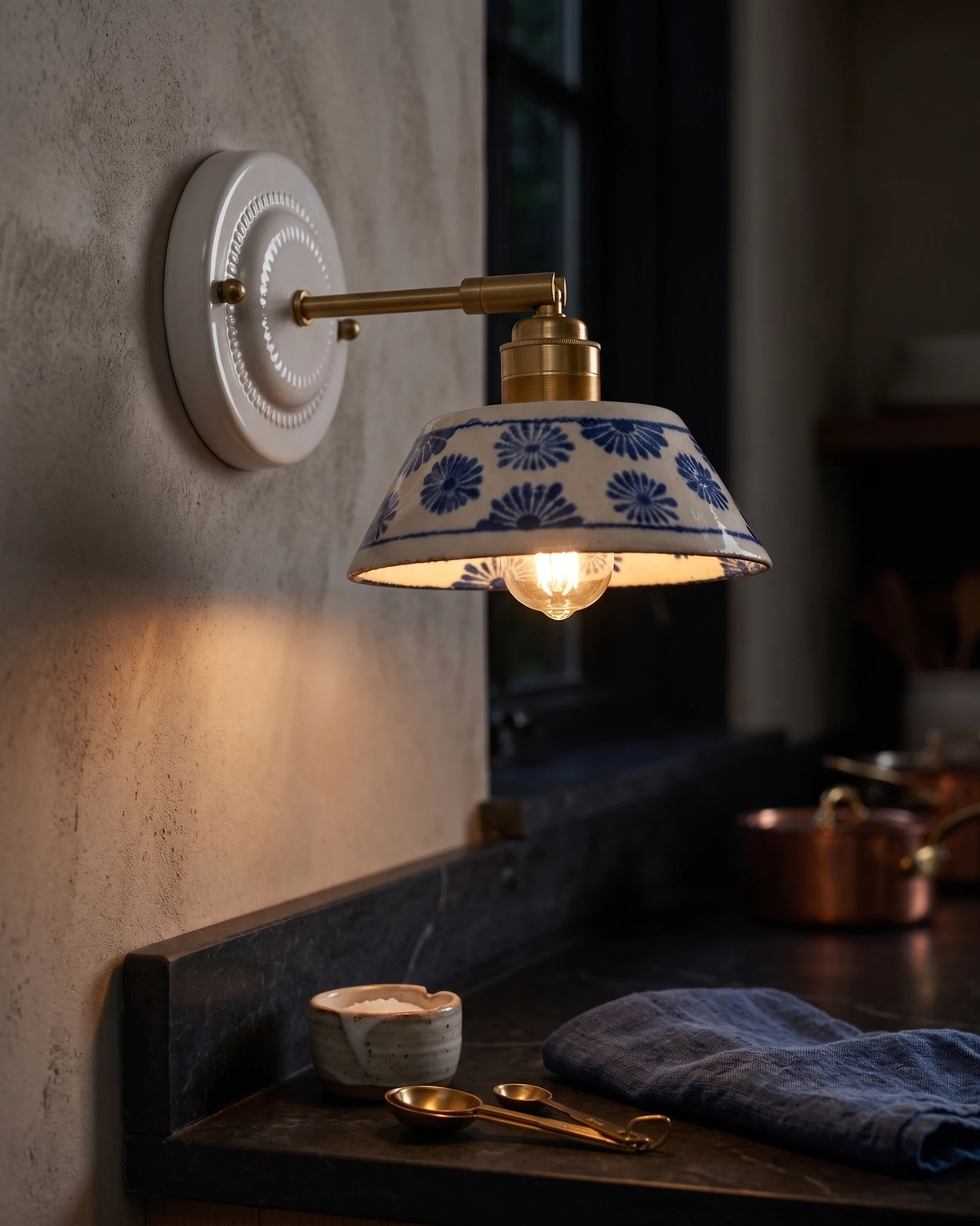 Ceramic wall sconce FIORA No.01 lit above a dark wood counter by a window