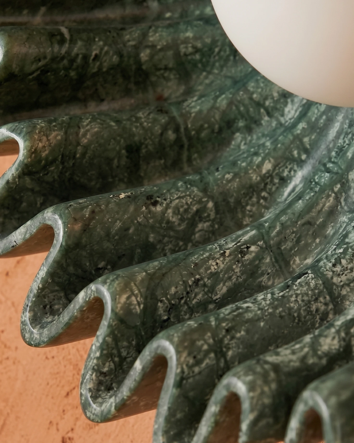 Extreme close-up of the mottled green glaze on the sculpted ceramic rays of the RAGGI No.01 ceramic wall sconce