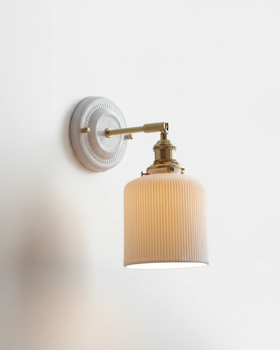 Ceramic wall sconce RIGA No.01 in White Ribbed Ceramic with Antique Brass, cylinder shade glowing on a swing arm