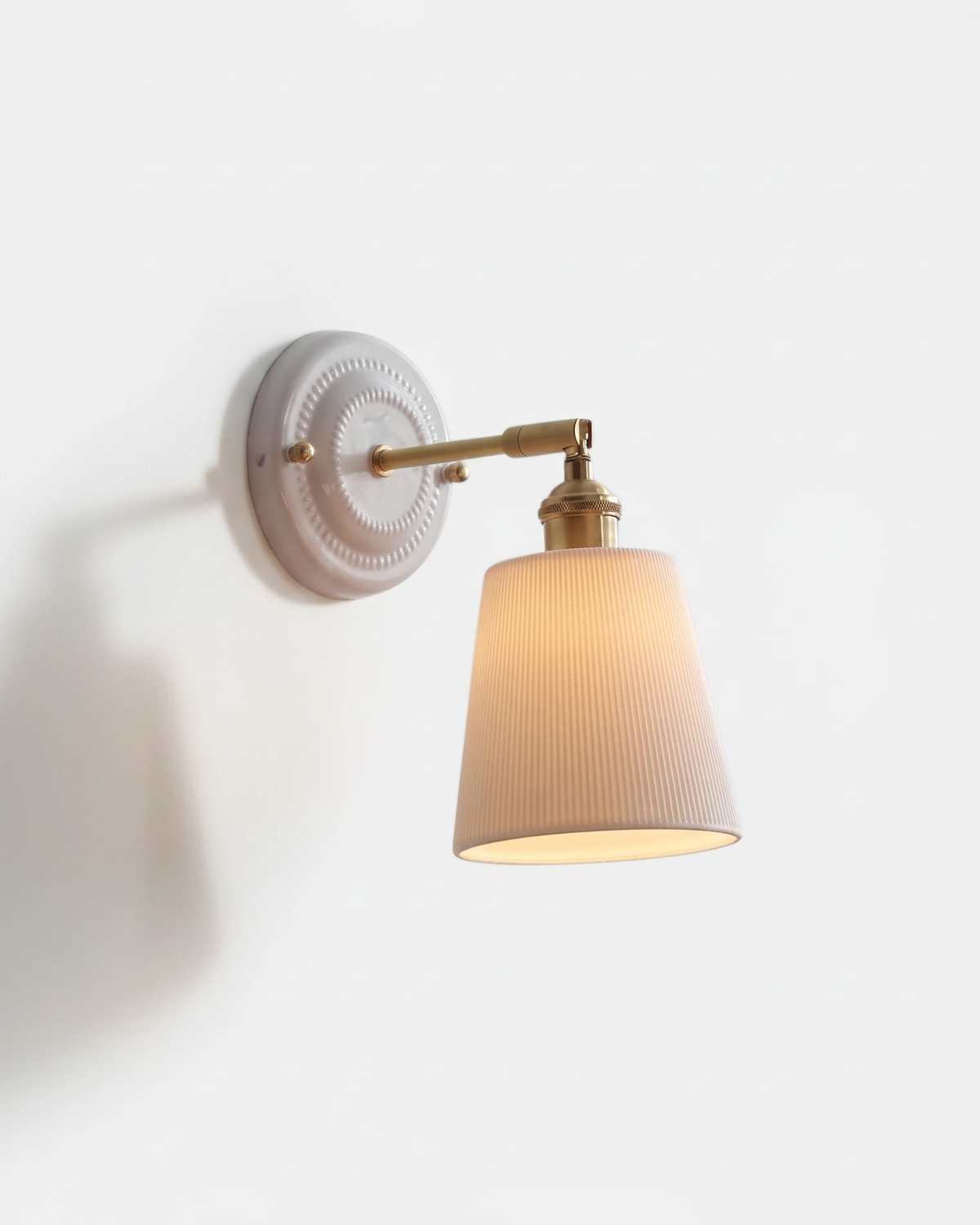 Ceramic wall sconce RIGA No.02, white ribbed tapered shade lit on an antique brass swing arm