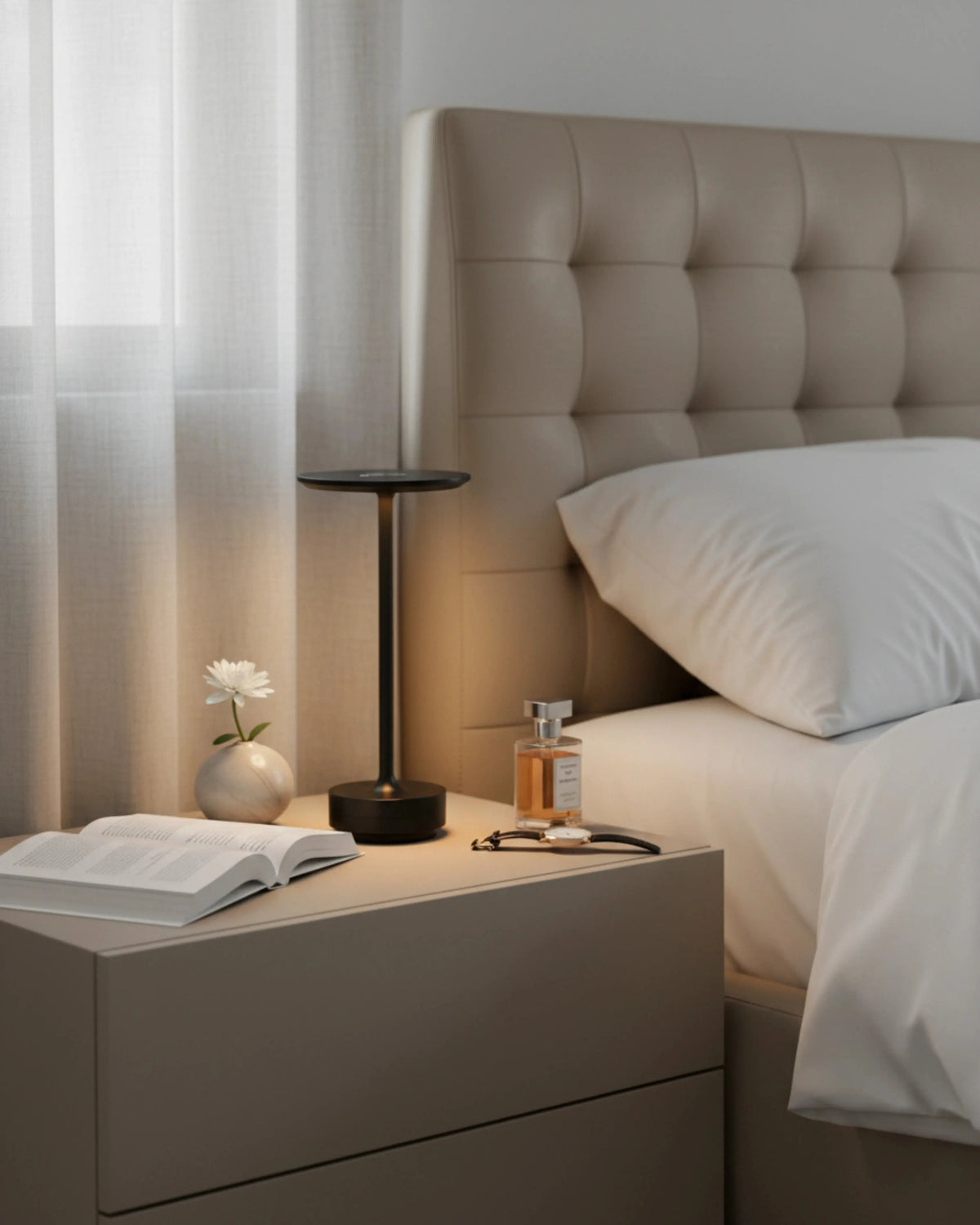 Cordless desk lamp LUMA No.05 in black lit on a nightstand beside a bed with a tufted headboard