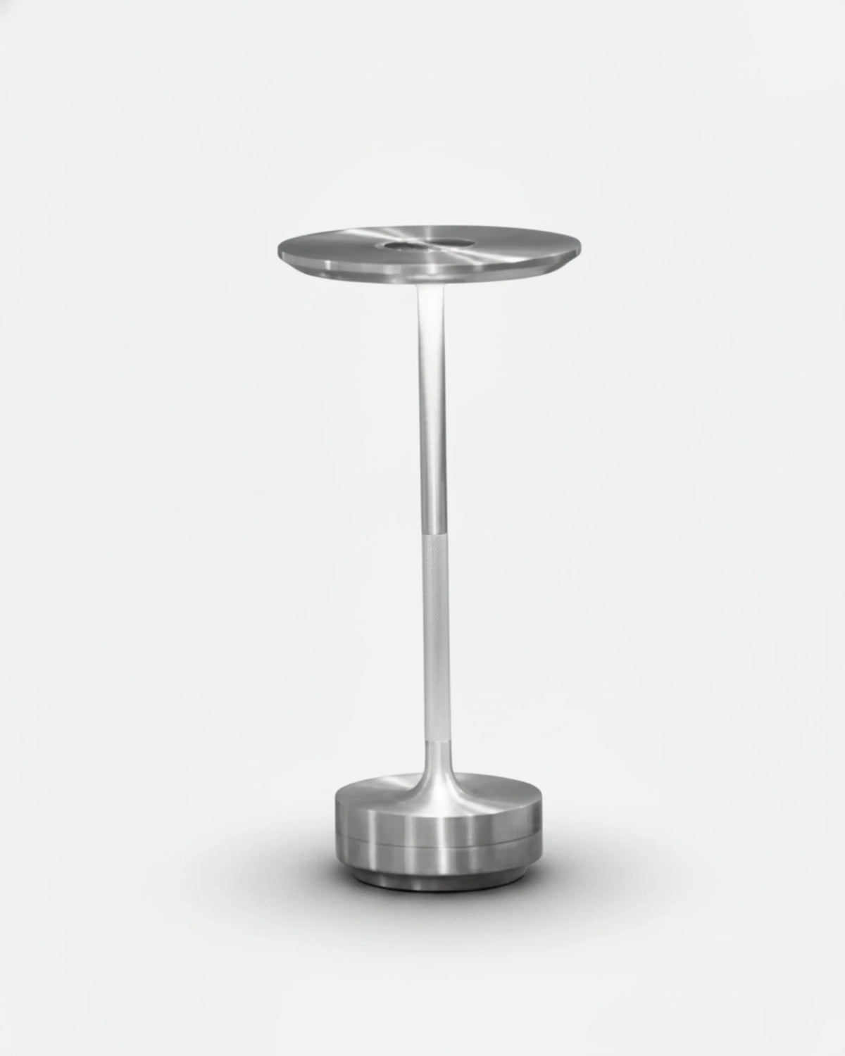 Cordless desk lamp LUMA No.05 in silver, disc top switched on, slim stem and round base on a white background