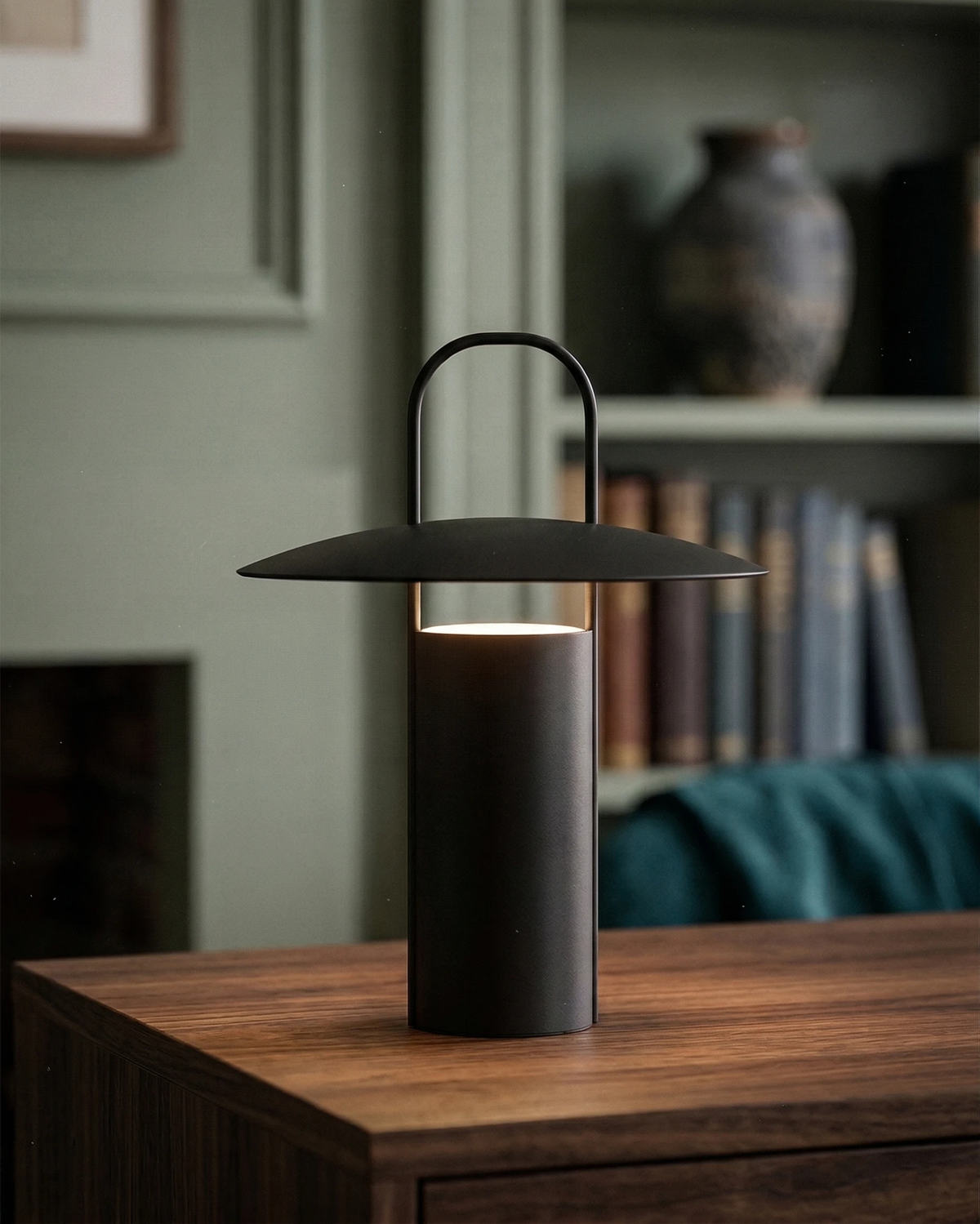 Cordless lantern lamp PORTO No.01 in black, lit on a walnut sideboard in front of bookshelves