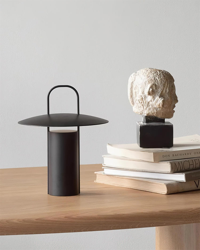 Cordless lantern lamp PORTO No.01 in black on a wooden table with stacked books and a stone bust