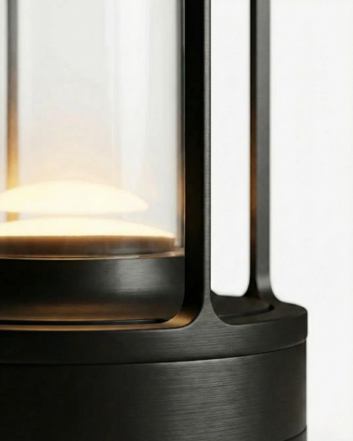 Close-up of the LATTA No.01 cordless lantern lamp in matte black, glass cylinder glowing above the base