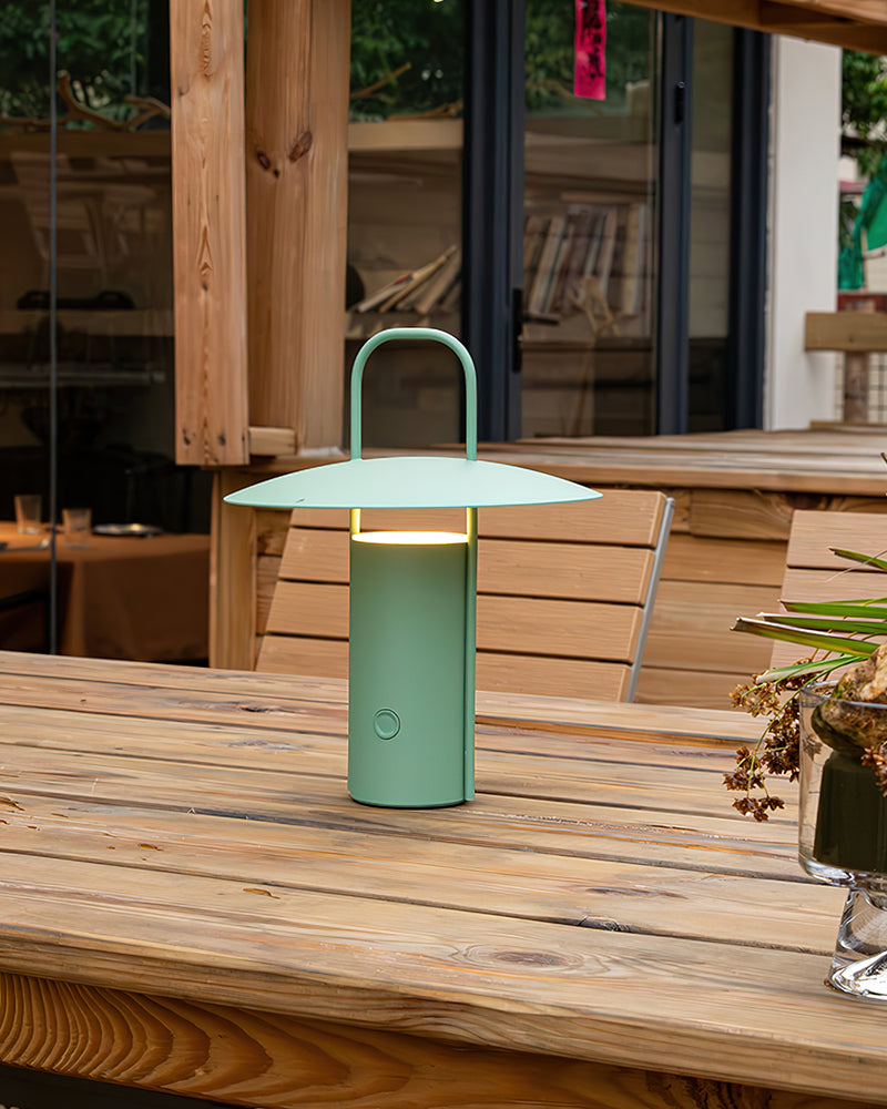 Cordless lantern lamp PORTO No.01 in forest green lit on a wooden table on a sunny deck