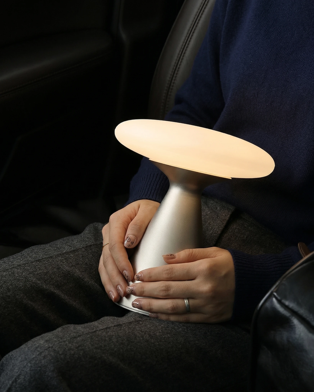 Cordless mushroom lamp DOMA No.03 lit and held in the lap of a seated person in a navy sweater