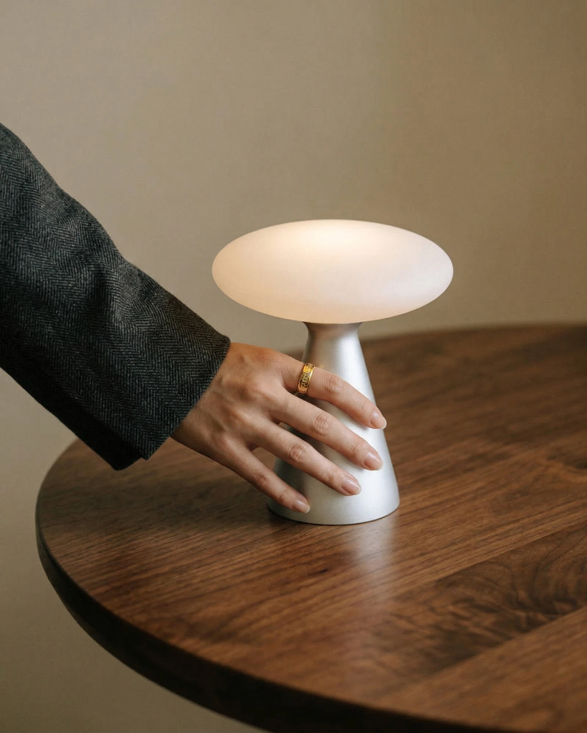 Hand reaching for the cordless mushroom lamp DOMA No.03 switched on atop a round walnut table