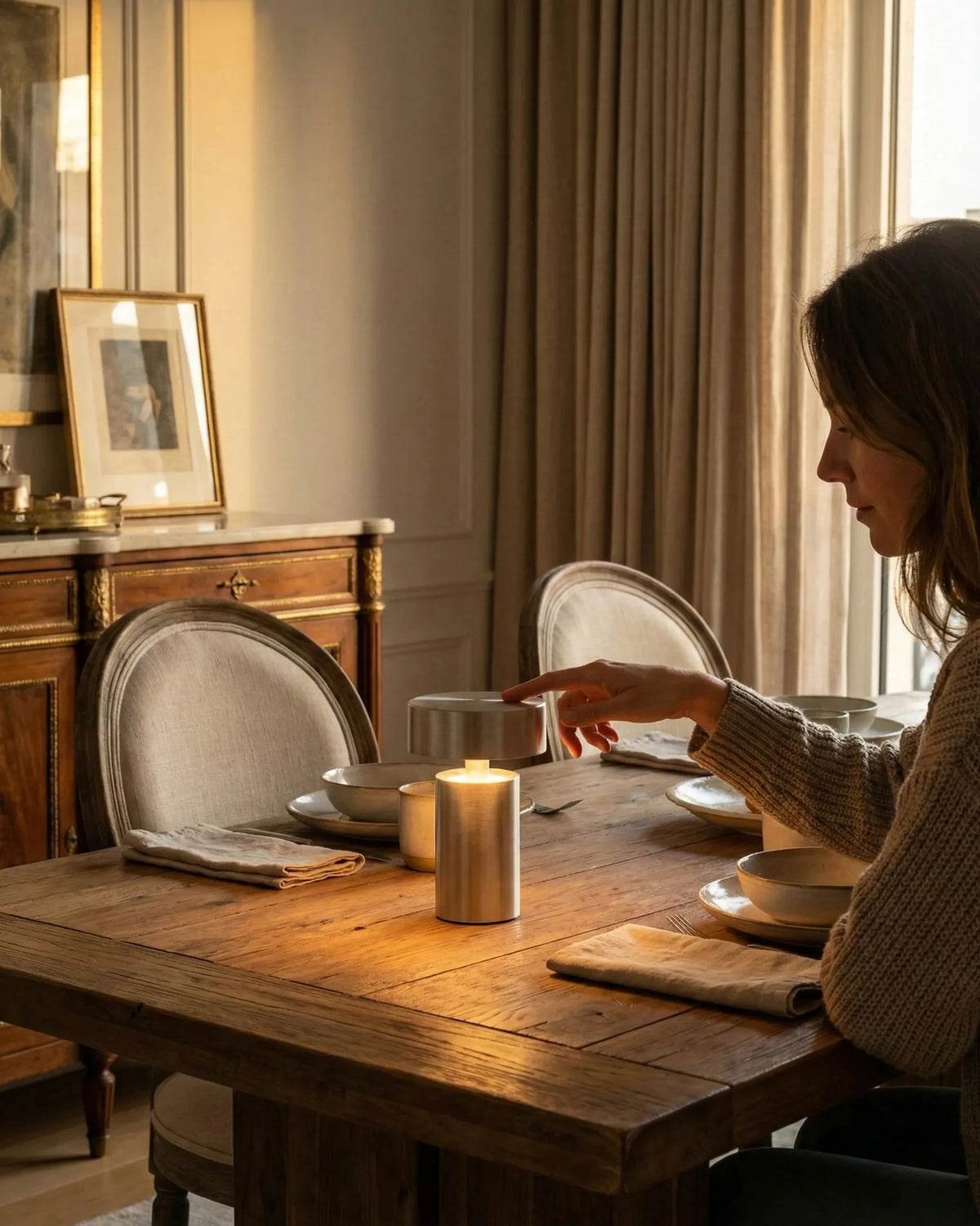 Cordless mushroom lamp PADOVA No.01 in brushed silver lit on a set wooden dining table, a woman reaching to touch it