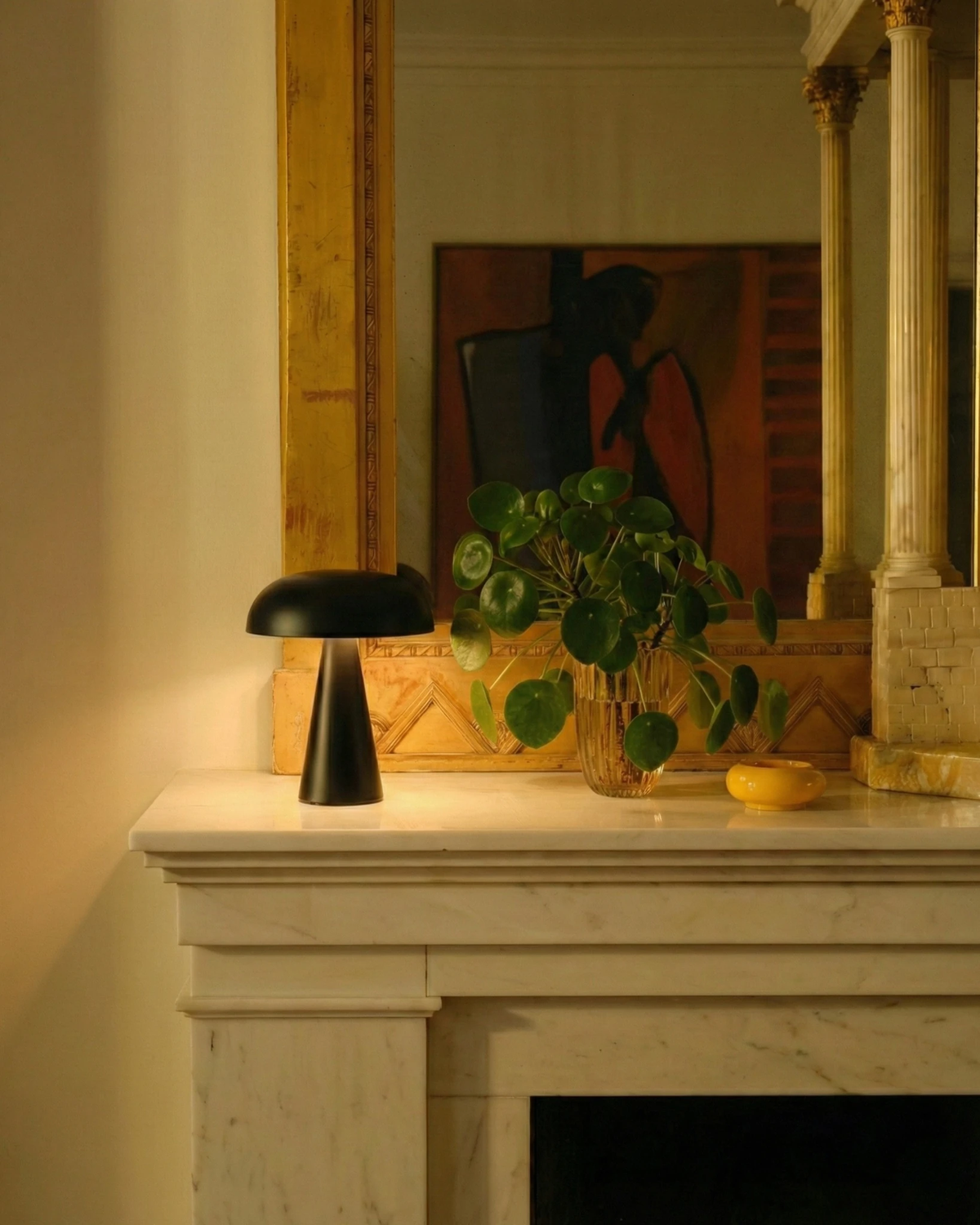 Cordless mushroom lamp LUMA No.04 in black lit on a marble mantel below a gilt mirror with a leafy plant