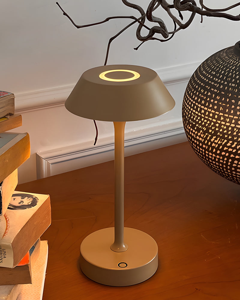 Cordless mushroom lamp CIMA No.01 in mustard yellow lit on a wooden table with stacked books and a branch
